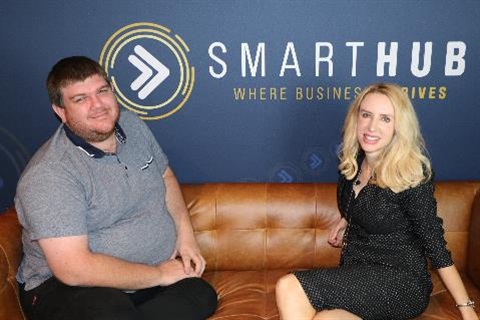 Photo of John Cook and Elize Hattin sitting on a tan coloured couch in front of SmartHub Rockhampton logo