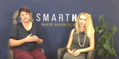 Natalie Nichols and Elize Hattin sitting in front of SmartHub logo wall